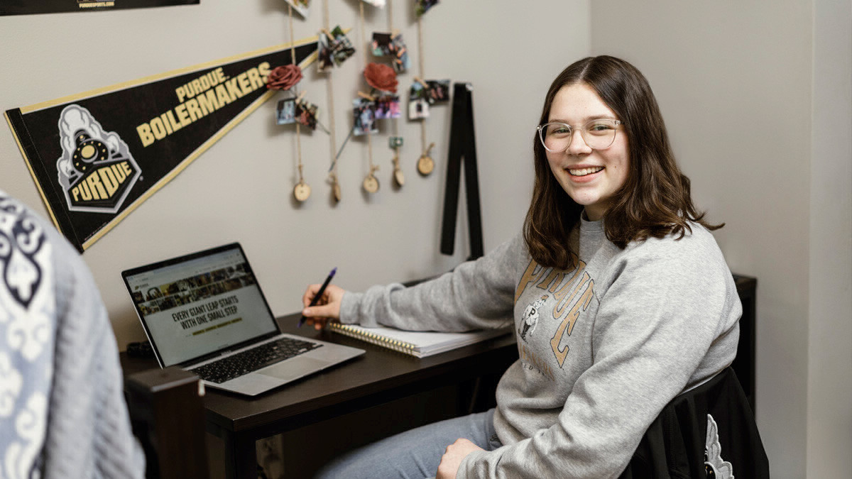 Student sitting at a decorated desk, looking at and smiling or the camera. 