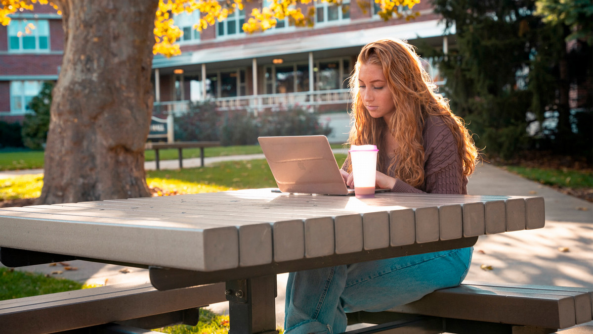 A student sitting at a table outside working on her laptop.