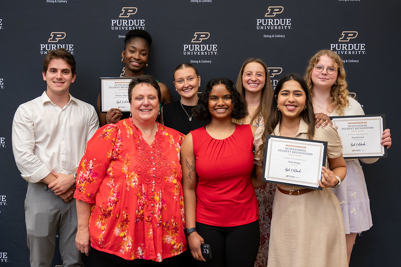 Students and staff smile in front of banner at Dining & Culinary banquet