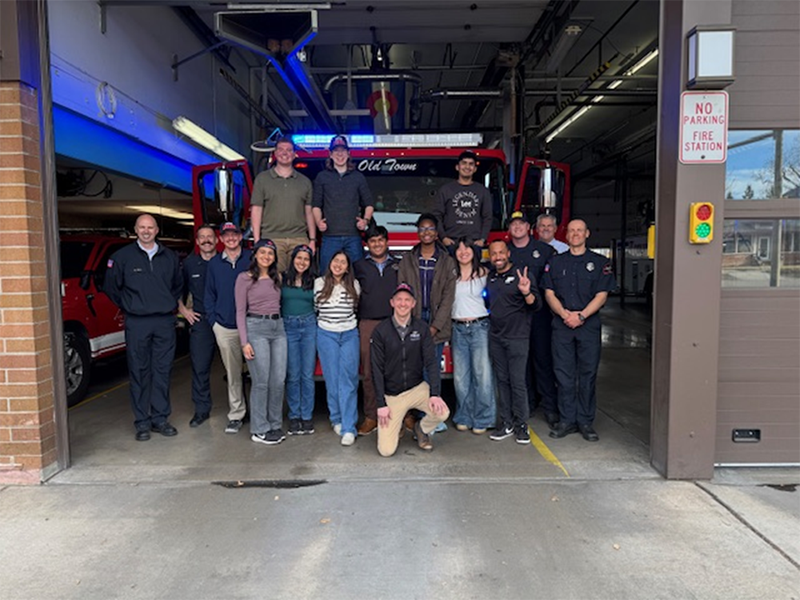 Students smiling in front of fire truck parked in fire station