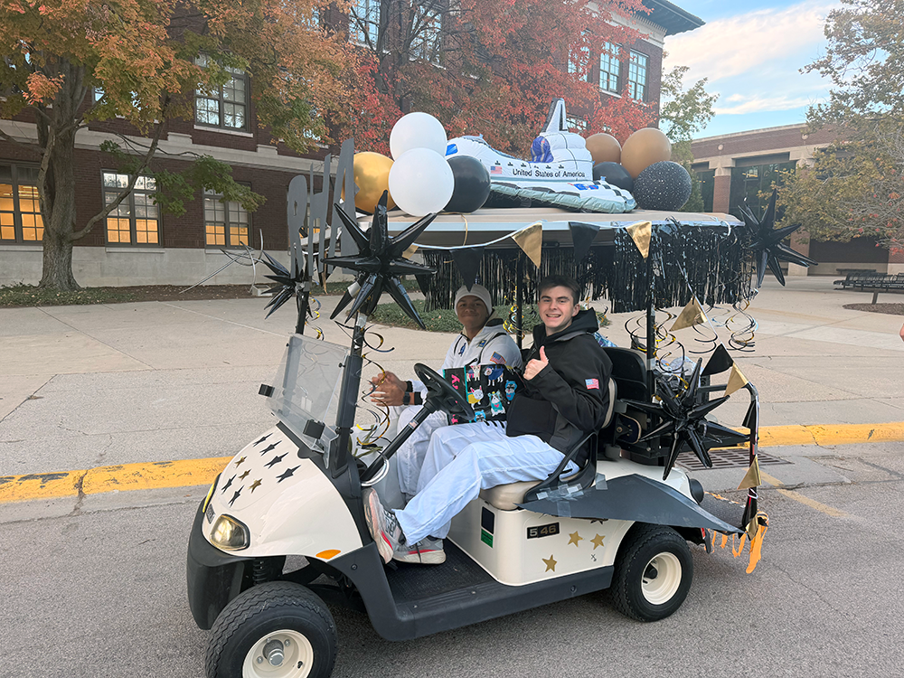 Students ride golf cart decorated with space theme. 